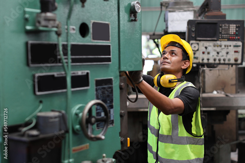 Technician engineer man in protective uniform standing and using computer monitor while controlling operation or checking industry machine process with hardhat at heavy industry manufacturing factory