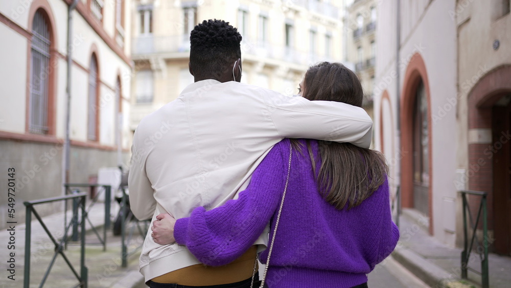 Interracial couple dating arms around body while walking outside in street