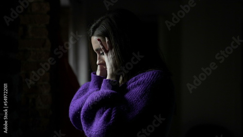 Concerned young woman standing by window at home. Anxious emotion