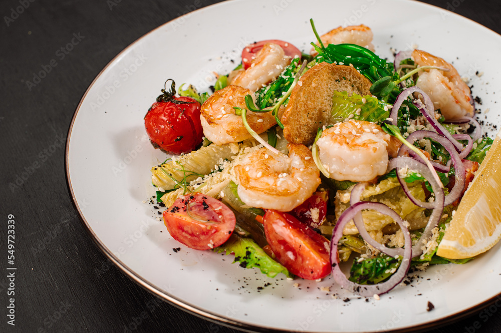 Tasty salad with shrimps, herbs and vegetables on black background