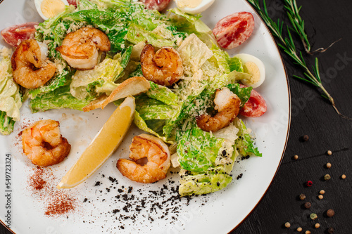 Tasty salad with shrimps, herbs and vegetables on black background