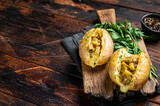 Kumpir, baked Jacket potatoes stuffed with cheese, bacon, salty cucumber, herbs and butter. Wooden background. Top view. Copy space