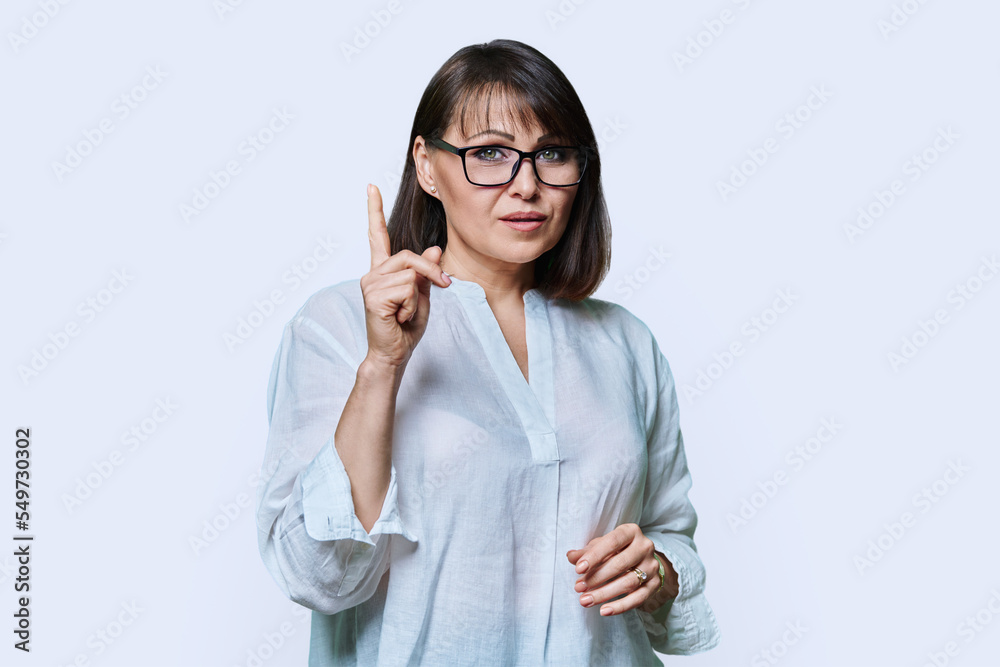 Middle aged serious woman showing index finger up, on white background Middle aged serious woman showing index finger up, on white background