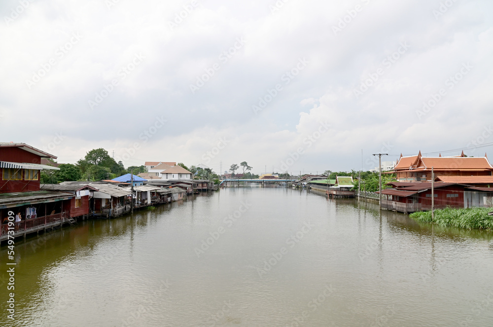 BANGKOK, THAILAND - NOVEMBER 20, 2022 : Wooden houses, Thai houses and buildings along the Chao Phraya River with white clouds and blue sky background, Town Ayutthaya Waterfront, Thailand.