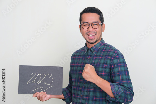 Adult Asian man holding a paper with year 2023 text with excited expression photo