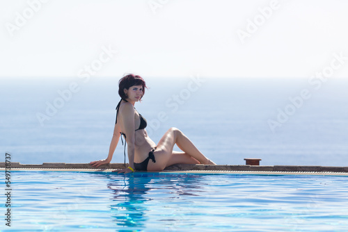 Woman bikini sitting on the edge of the pool  copy space.