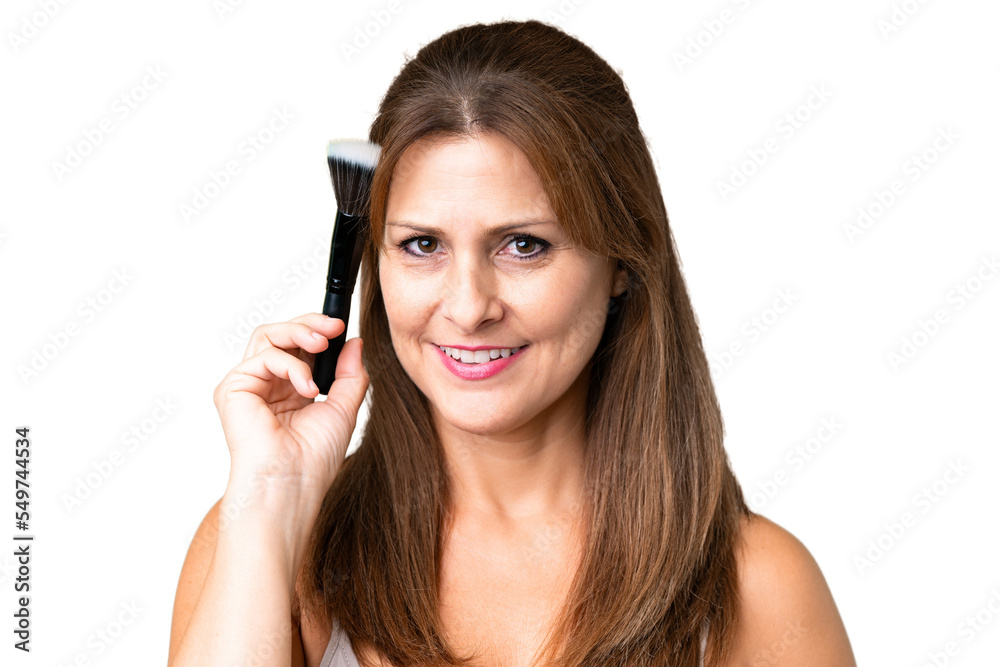 Middle age woman over isolated background holding makeup brush Middle age woman over isolated background holding makeup brush