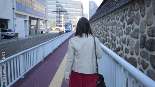 Back shot of asian girl walking by the stone wall in Nagasaki Japan. A train passes by. photo