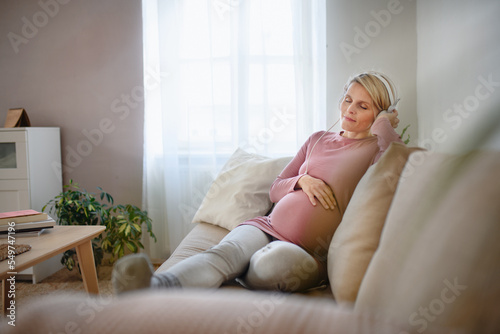 Pregnant woman sitting in her bed, listening music and enjoying time for herself.