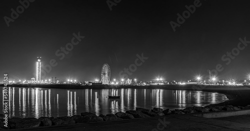 The great mosque and ferris wheel seen from Sablettes beach in the dark night. Skyline view of Algiers city, water reflexion lights illuminated by world biggest minaret. A motion blur boat floating 