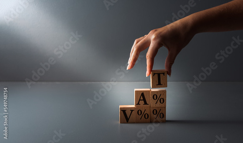 hand posing wooden blocks with vat or value added tax . concept of paying taxes , on grey background .