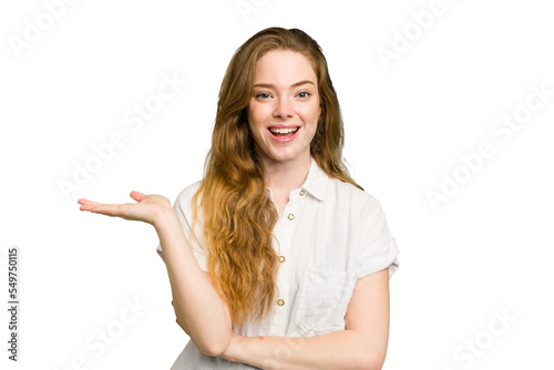 Young caucasian redhead woman isolated showing a copy space on a palm and holding another hand on waist.