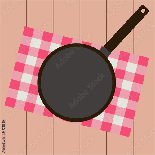 Simple flat black empty frying pan on a traditional red napkin and brown wooden table background