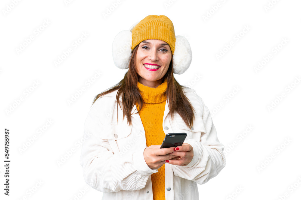 Middle age woman wearing winter muffs over isolated chroma key background sending a message with the mobile Middle age woman wearing winter muffs over isolated chroma key background sending a message with the mobile