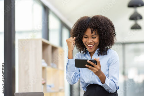 Successful and exciting Young african american business woman looking at the phone screen  african woman excited to win on her smartphone at work.