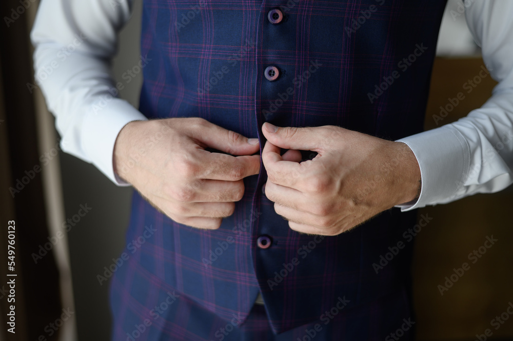 Obraz premium Portrait of a fashionable man fastening a button on jacket, close-up.Wedding day