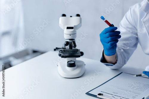 Lab assistant, a medical scientist, a chemistry researcher holds a glass tube through the blood sample, does a chemical experiment and examines a patient's blood sample. Medicine and research concept.
