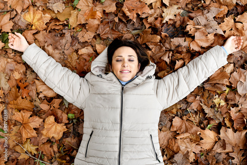 middle-aged woman lying on a pile of dry tree leaves in autumn. concept enjoy the field in autumn. weekend free time