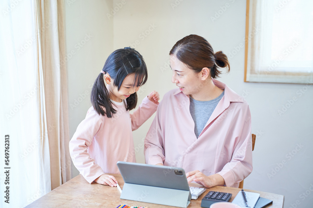 自宅でパソコンに向かう母親に寄り添う女の子 自宅でパソコンに向かう母親に寄り添う女の子