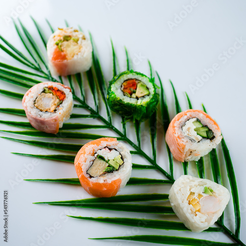 Fresh sushi rolls with rice, avocado, crab stick, shrimp tempura, tofu, Japanese omelette, chives, salmon, seaweed, nuts and sauce on palm leaf.