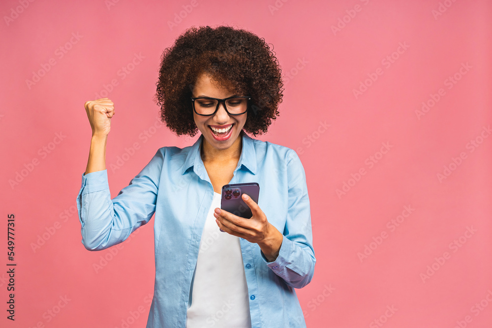 Image of a happy emotional african american woman posing isolated over pink background using mobile phone make winner gesture. Image of a happy emotional african american woman posing isolated over pink background using mobile phone make winner gesture.