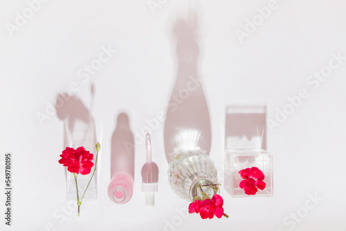 Cosmetic bottle with pipette and pink liquid. Surrounded by pink flowers. On a light background.