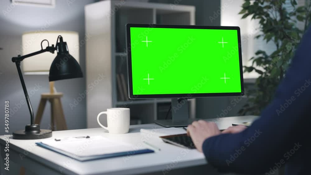 Businessman in formal clothes working on computer with chroma screen, blank green copy space in evening office interior