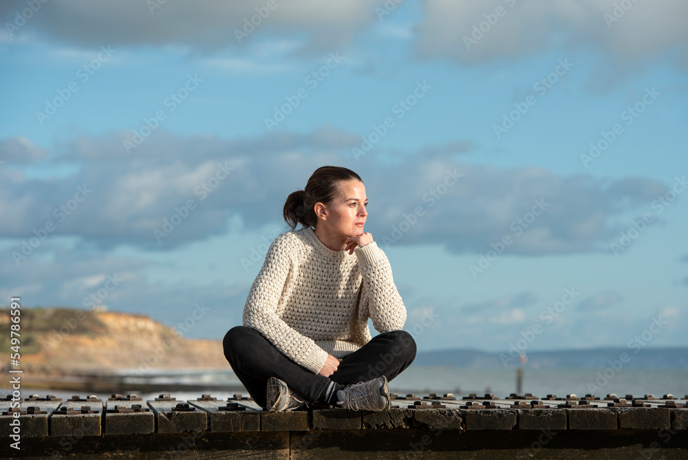 woman sitting outdoors by the ocean, enjoying the view. Looking thoughtful. woman sitting outdoors by the ocean, enjoying the view. Looking thoughtful.