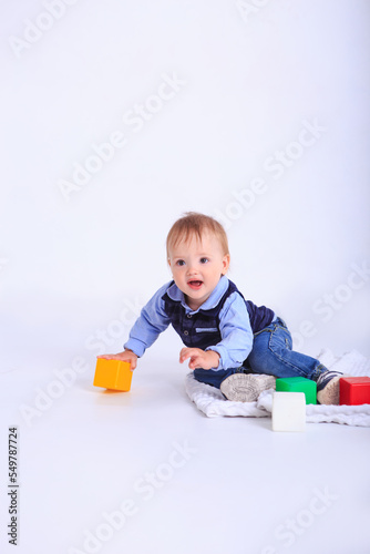 A little boy plays with colored dice on a white background. Studio shot of a child playing.