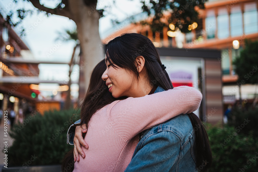 Fototapeta premium Two laughing young women hugging each other at a shopping center