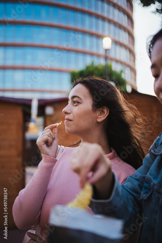 Two happy girls eating potato chips while are having fun at a shopping center