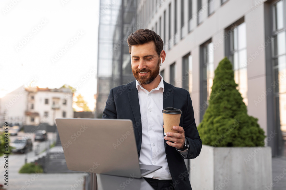 Happy confident young european man boss with beard in suit, wireless headphones typing on computer Happy confident young european man boss with beard in suit, wireless headphones typing on computer