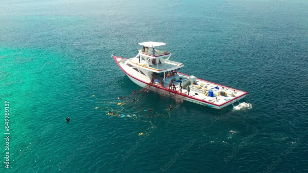 Fishermen on a white boat take out fishing nets with caught fish near a local island in the Maldives. Aerial drone view turquoise sea.