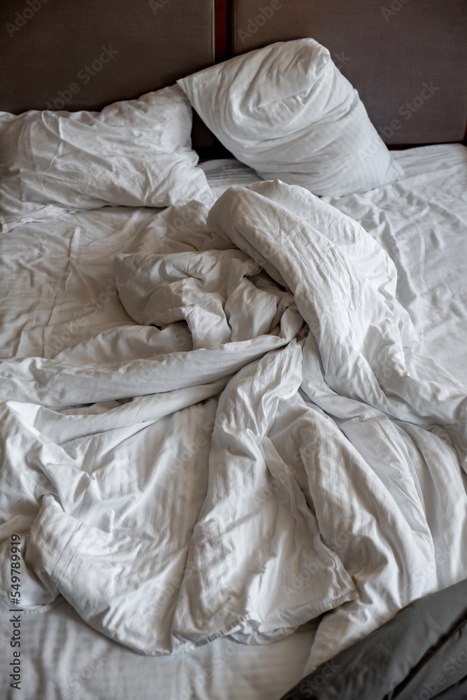 pillows and blankets lie on the bed in an improper form; unmade bedding on the bed; white bed linen