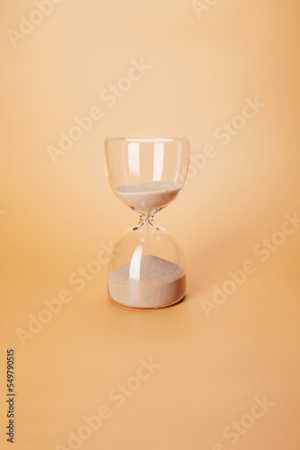 Hourglass with clean sand pouring down countdown the time, isolated on the bright solid fond plain sandy beige background