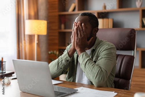 Tired sad middle aged african american guy covers face with hands suffering from overwork