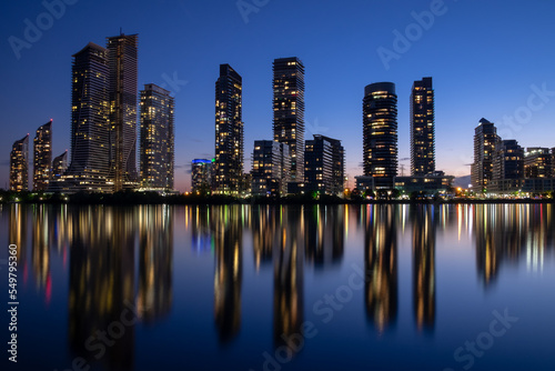Night cityscape of buildings  towers  skyscrapers with beautiful colorful electric lights reflection in still water surface. Long exposure shot. Toronto  Canada. Space for copy. Condo market concept.