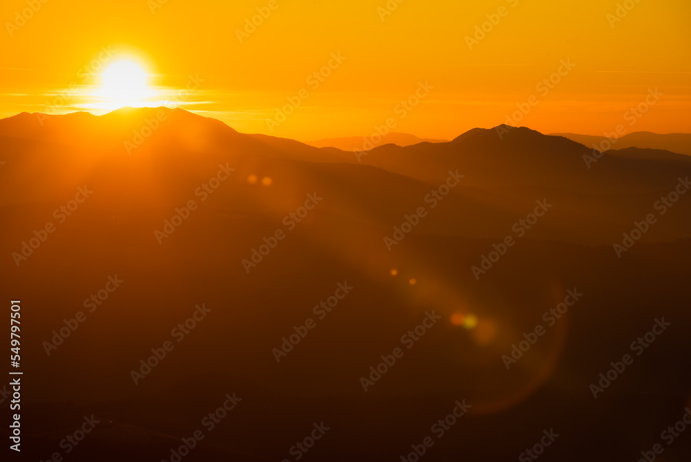 Orange and yellow sunset with mountains silhouettes. Gradient vivid nature background.
