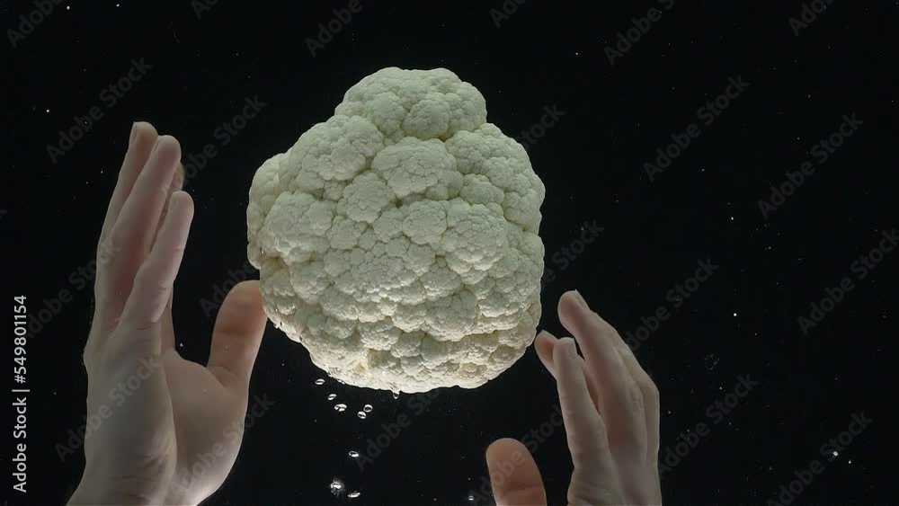 Close-up of cauliflower falling into the water in a slow motion. Сauliflower in hands.