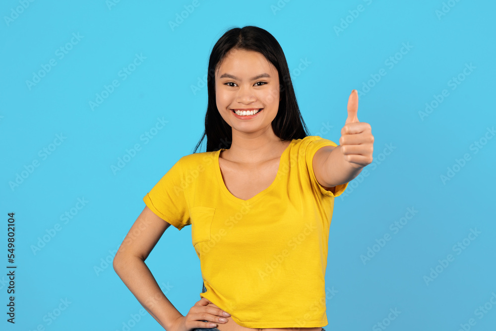 Satisfied millennial japanese lady student in yellow t-shirt show thumb up and look at camera Satisfied millennial japanese lady student in yellow t-shirt show thumb up and look at camera
