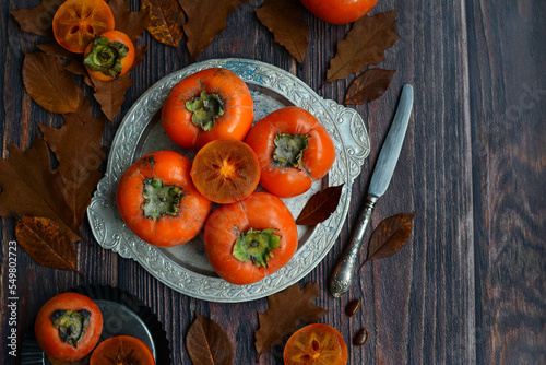Ripe persimmon fruits on a plate, top view. Wooden background, copy space