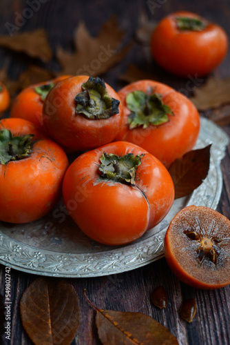 Close up of ripe orange persimmons on a silver platter. Vertical.