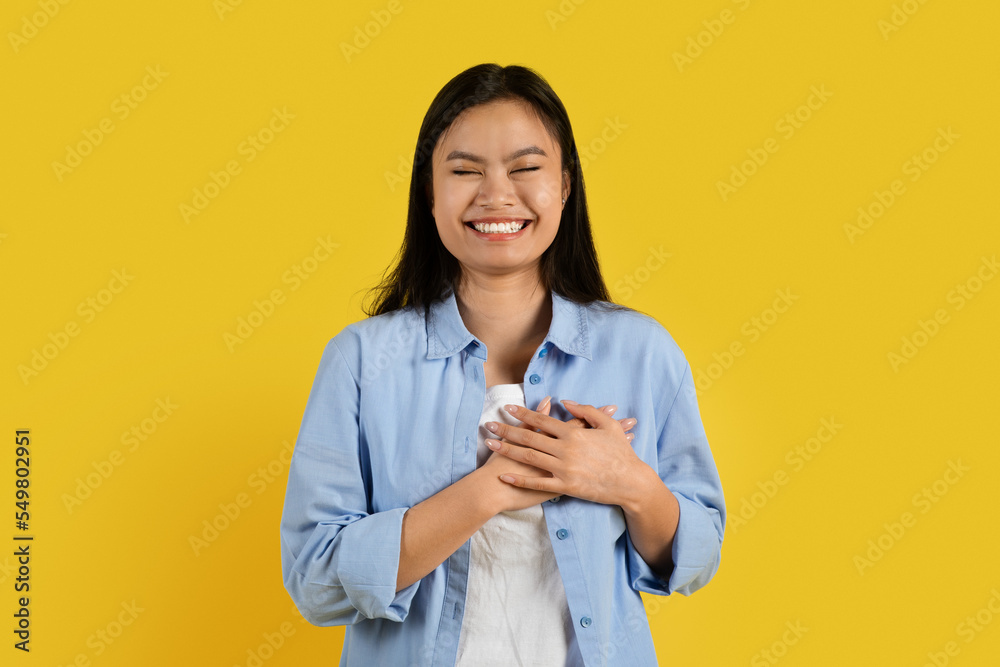 Cheerful cute millennial asian lady with down syndrome in casual presses hands to chest Cheerful cute millennial asian lady with down syndrome in casual presses hands to chest