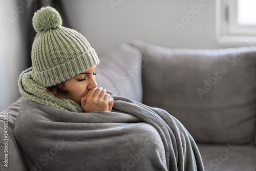 Fotografia Freezing Woman Warming Hands With Breath While Sitting On Couch At Home