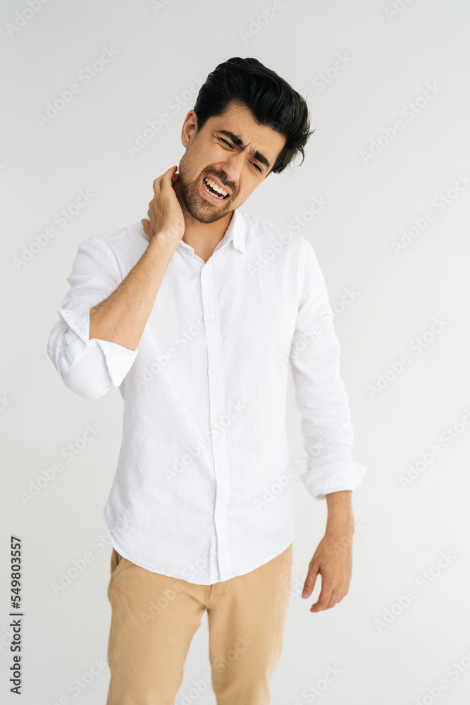Vertical portrait of tired bearded man feeling physical discomfort massaging tensed muscles, having painful neck hurt shoulder ache, standing on white isolated background. Negative face expression. Vertical portrait of tired bearded man feeling physical discomfort massaging tensed muscles, having painful neck hurt shoulder ache, standing on white isolated background. Negative face expression.