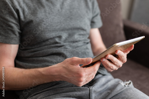 Man sitting on a couch and reading something on a tablet. Using technology.