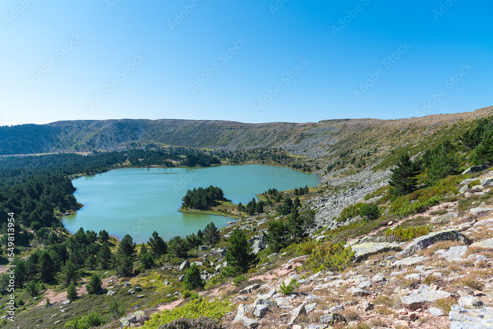 Beautiful view of a lake surrounded by greenery mountains and trees under a blue sky, Neila Lagoons Natural Park, Burgos, Spain
