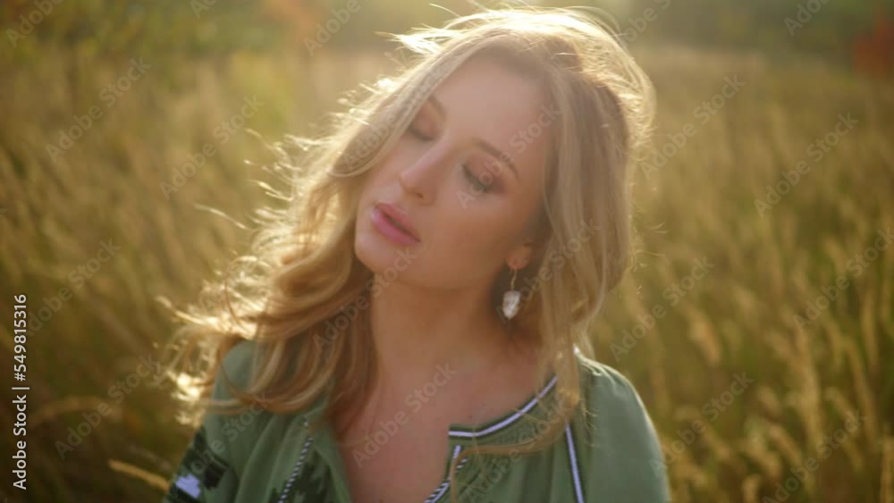 Beautiful young woman dances at wheat field, moving with the wind. Enigmatic tender face, blond hair. View of embroidered green dress, blurred stems, sunshine. Non urban background. High quality 4k Beautiful young woman dances at wheat field, moving with the wind. Enigmatic tender face, blond hair. View of embroidered green dress, blurred stems, sunshine. Non urban background. High quality 4k