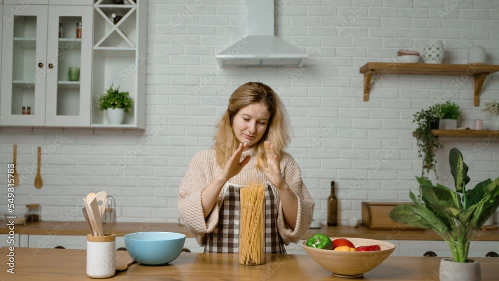 A housewife cleans the kitchen and puts dry spaghetti in a glass container for storage. Organization of kitchen space. Storage of ingredients and cereals. Environmentally friendly glass jar container A housewife cleans the kitchen and puts dry spaghetti in a glass container for storage. Organization of kitchen space. Storage of ingredients and cereals. Environmentally friendly glass jar container