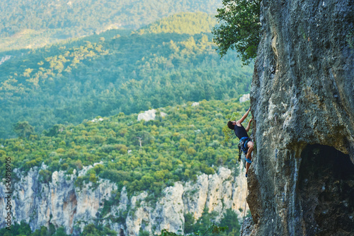 Panoramic view of beautiful mountains and rocks, active strong man climbing on high vertical cliff wall